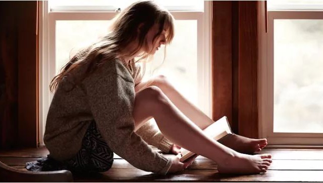 Woman reading a book in a window.