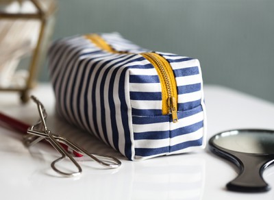 Striped makeup bag and eyelash curlers on a desk.
